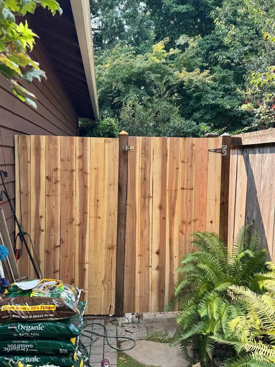 A newly built cedar gate hung between posts beside an older weathered fence