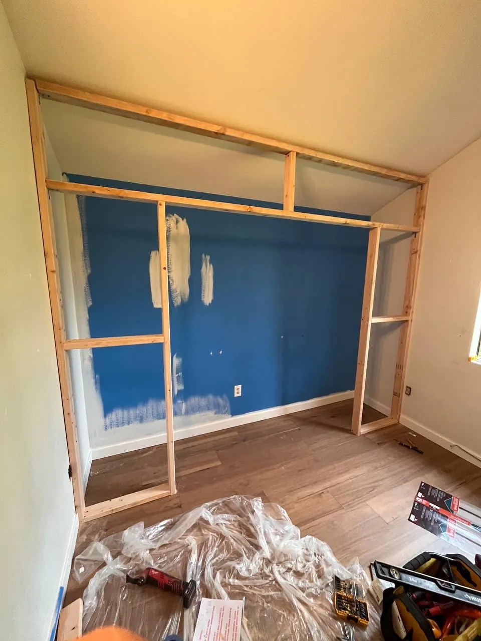 New wood framing for a closet standing in front of a blue bedroom wall