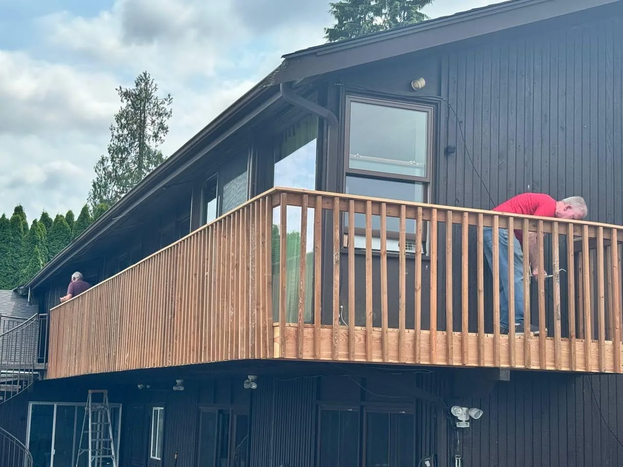 Two of the crew fitting a cedar railing along a second-storey balcony