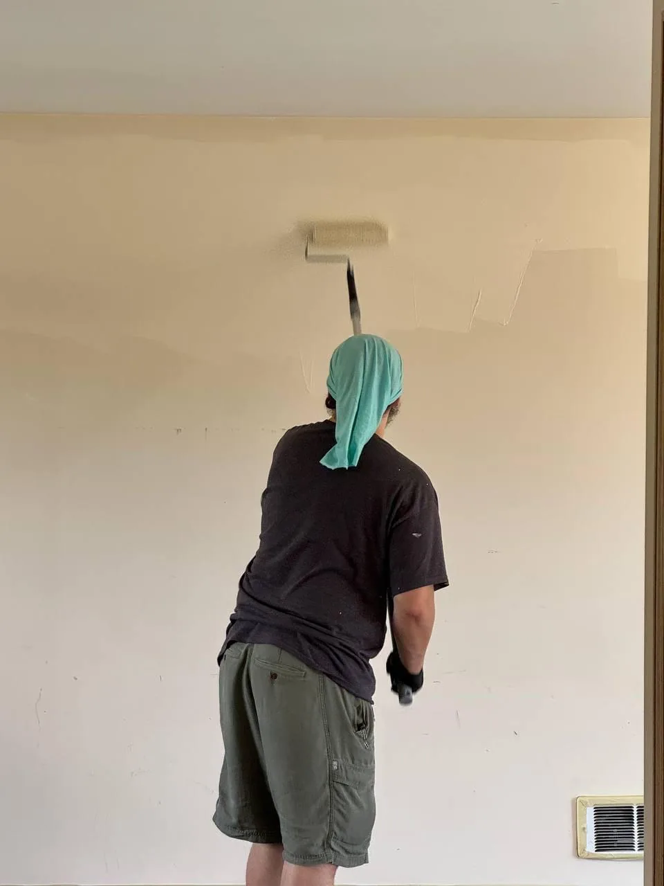 A painter rolling the top of a wall, seen from behind