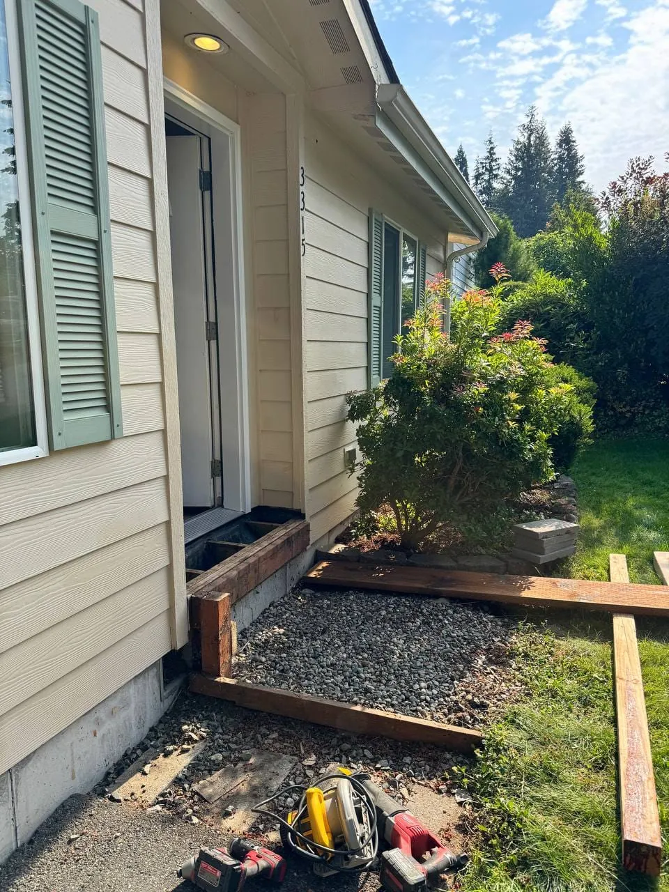 The porch area cleared by the front door, new lumber laid out on the lawn