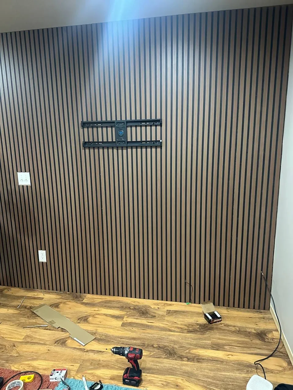 A TV wall bracket fixed to a slatted wood wall, drill on the floor
